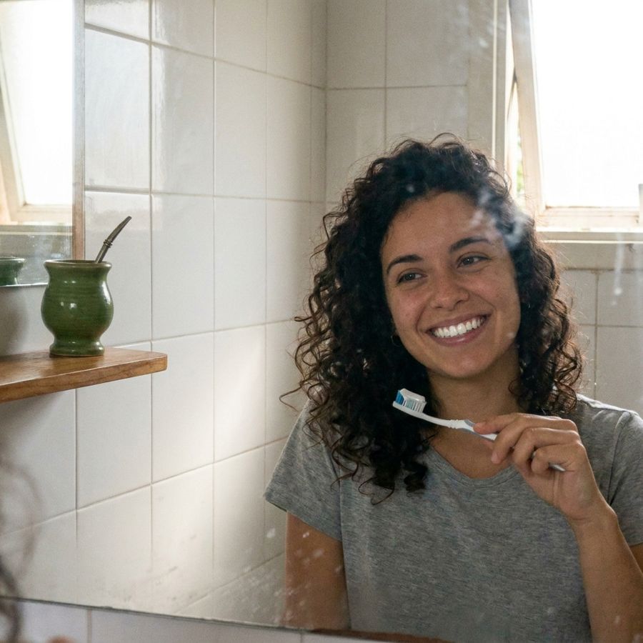 Chica cepillándose frente al espejo, sonriendo